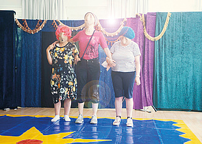 Die Theatergruppe für ihren Auftritt. Drei Teilnehmerinnen stehen verkleidet auf der Bühne. Beim Abschlussfest zeigen alle Workshop-Gruppen, was sie gemacht haben.
