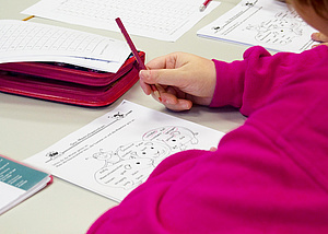 Eine Teilnehmerin sitzt an einem Tisch. Vor ihr liegen mehere Arbeitsblätter und ein Federpenal. Sie hält einen Stift in der Hand. Auf dem Blatt kann man sehen, dass sie ein paar Wörter eingekreist hat.