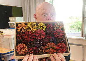 Ein Teilnehmer zeigt stolz sein Kunstwerk. Eine kleine Kiste gefüllt mit bunt bemalten Bockerln.