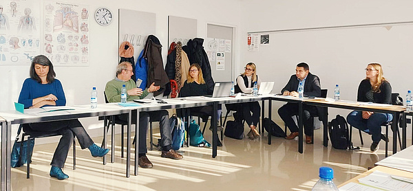Bei dem Erasmus Projekttreffen in Wien. Die Projektpartnerinnen und Projektpartner sitzen an langen Tischen und sind fleißig an der Arbeit.