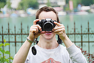 Ein Teilnehmer beim Fotoworkshop. Er steht direkt am Ufer des Wolfgangsees und hält sich die Kamera vors Gesicht um ein Foto zu machen.
